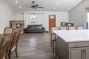 Interior space with ceiling fan, a stone fireplace, a kitchen breakfast bar, and dark hardwood / wood-style floors