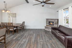 Living room featuring ceiling fan with notable chandelier, dark wood-type flooring, vaulted ceiling with beams, and a fireplace