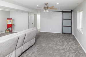 Living room featuring a barn door, ceiling fan, and dark carpet