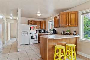 Kitchen featuring a healthy amount of sunlight, kitchen peninsula, white appliances, and light tile floors