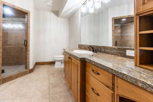 Bathroom featuring a shower with shower door, toilet, large vanity, and tile floors