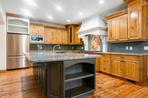 Kitchen featuring appliances with stainless steel finishes, light hardwood / wood-style flooring, tasteful backsplash, and an island with sink