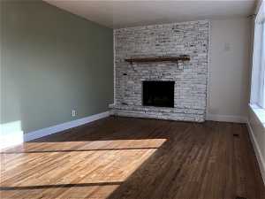 Unfurnished living room featuring wood-type flooring, brick wall, and a fireplace