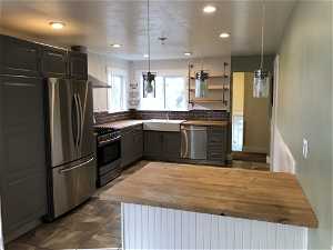 Kitchen with butcher block countertops, appliances with stainless steel finishes, tasteful backsplash, and decorative light fixtures
