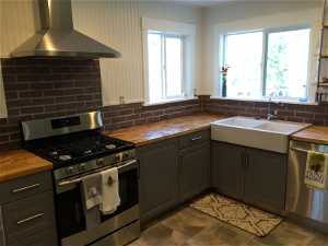 Kitchen with wall chimney range hood, stainless steel appliances, and butcher block countertops