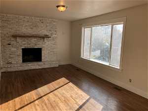 Unfurnished living room featuring a healthy amount of sunlight, dark wood-type flooring, and a brick fireplace