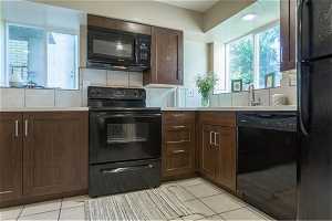 Kitchen featuring tasteful backsplash, light tile floors, and black appliances