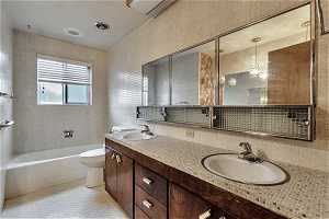 Full bathroom with double sink vanity, backsplash, toilet, tile floors, and  shower combination