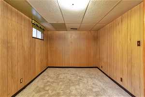 Basement with light colored carpet, a paneled ceiling, and wooden walls