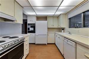 Kitchen with sink, white appliances, backsplash, light hardwood / wood-style floors, and tile counters