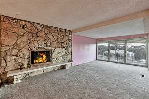 Unfurnished living room with a textured ceiling, carpet floors, and a stone fireplace