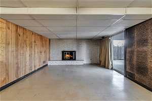 Unfurnished living room with a fireplace, brick wall, a paneled ceiling, and wooden walls