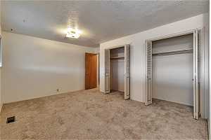 Unfurnished bedroom featuring light colored carpet, a textured ceiling, and multiple closets