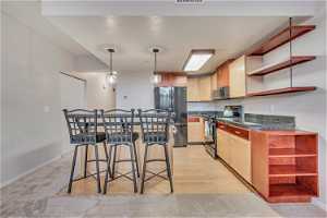 Kitchen with stainless steel appliances, light carpet, a breakfast bar, and decorative light fixtures