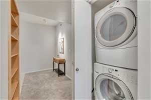 Laundry area featuring light colored carpet and stacked washer / drying machine