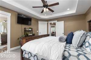 Carpeted bedroom with ensuite bath, ceiling fan, and a tray ceiling