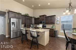 Kitchen with light stone countertops, dark hardwood / wood-style floors, appliances with stainless steel finishes, a center island with sink, and vaulted ceiling