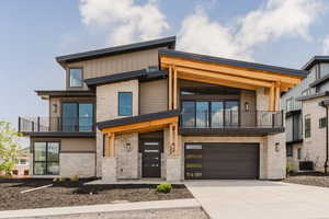 Contemporary home featuring stone siding, a balcony, driveway, and an attached garage