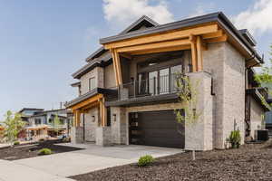 Contemporary house featuring stone siding, a balcony, concrete driveway, and an attached garage