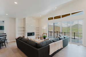 Living room featuring light wood finished floors, recessed lighting, a stone fireplace, built in shelves, and vaulted ceiling