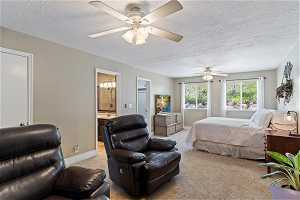Bedroom with ensuite bath, a textured ceiling, ceiling fan, and light carpet