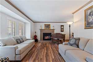 Living room with wood-style floors, a tiled fireplace, and ornamental molding