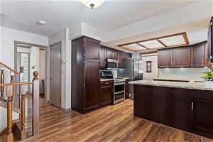 Kitchen featuring light stone countertops, dark brown cabinets, stainless steel appliances, hardwood / wood-style flooring, and tasteful backsplash