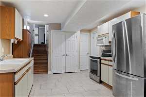Kitchen with sink, appliances with stainless steel finishes, white cabinetry, and light tile floors