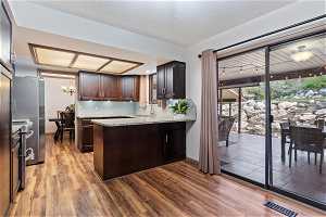 Kitchen featuring light wood-type flooring, kitchen peninsula, dark brown cabinets, light stone counters, and tasteful backsplash