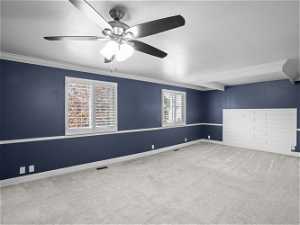 Carpeted empty room featuring plenty of natural light, crown molding, and ceiling fan