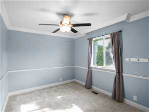 Carpeted spare room featuring ceiling fan and crown molding