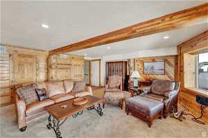 Living room featuring light colored carpet, beam ceiling, wood walls, and a textured ceiling