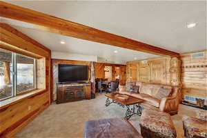 Living room featuring wood walls, carpet, beam ceiling, and a textured ceiling