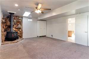 Large room featuring a skylight, a wood stove, ceiling fan, and carpet floors