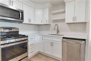 Kitchen with appliances with stainless steel finishes, light hardwood (LVP) / wood-style flooring, white cabinets, and sink