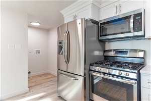 Kitchen featuring light hardwood (LVP)/ wood-style floors, appliances with stainless steel finishes, and white cabinetry