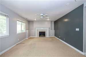 Unfurnished living room with a tiled fireplace, light carpet, and ceiling fan
