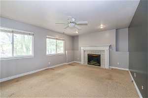 Unfurnished living room featuring light colored carpet, ceiling fan, and a tile fireplace