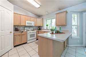 Kitchen featuring white appliances, plenty of natural light, kitchen peninsula, sink, and light tile floors