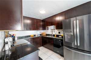 Kitchen featuring dark brown cabinetry, light tile floors, range, dishwasher, and stainless steel refrigerator with ice dispenser.