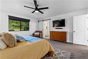 Carpeted bedroom with ceiling fan, connected bathroom, and a barn door