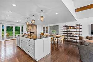 Kitchen with dark stone countertops, dark hardwood / wood-style floors, a center island with sink, and white cabinets