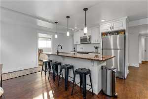 Kitchen with dark wood-type flooring, stainless steel appliances, white cabinets, and decorative light fixtures