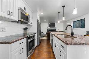 Kitchen with white cabinets, sink, backsplash, dark wood-type flooring, and stainless steel appliances