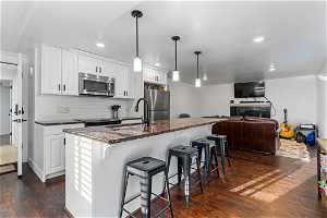 Kitchen with appliances with stainless steel finishes, white cabinets, backsplash, dark hardwood / wood-style flooring, and pendant lighting
