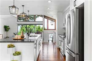 Kitchen with stainless steel appliances, dark wood-type flooring, dark stone countertops, sink, and pendant lighting