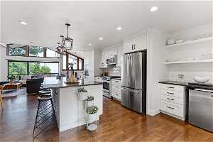 Kitchen with white cabinets, stainless steel appliances, dark wood-type flooring, and a kitchen bar