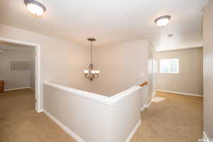 Hallway with light carpet and a chandelier