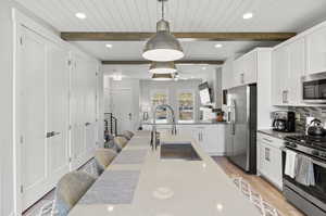 Kitchen with beamed ceiling, appliances with stainless steel finishes, light hardwood / wood-style floors, tasteful backsplash, and pendant lighting