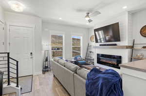 Living room with light hardwood / wood-style floors, ceiling fan, and a fireplace